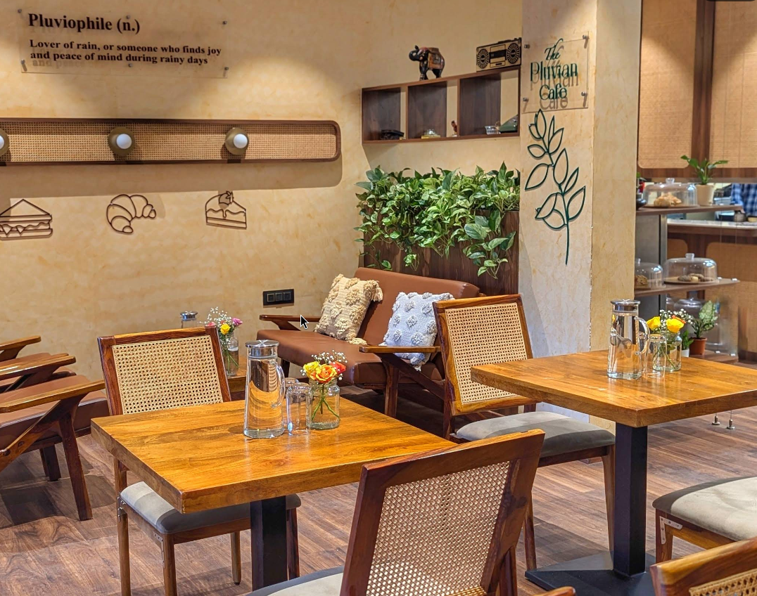The Pluvian interior — wooden tables, rattan chairs, warm lighting, and lush green plants